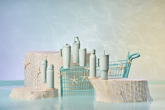 Seven assorted bottles arranged across rocky pillars in a beachy environment, with water and shells