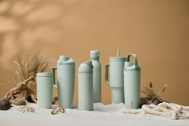 Six assorted summer bottles in the sand with shells, rope, and wheat scenic elements