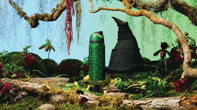 Shot of green water bottle next to the official hat from the movie, in a forest-inspired scene