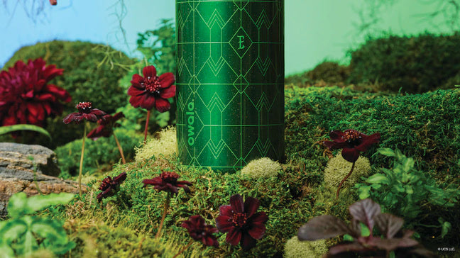 Shot of the bottom of the Elphaba bottle, sitting in a grassy background with dark flowers